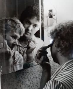 Gail Sheffield oversees a client using a mirror to put on makeup.