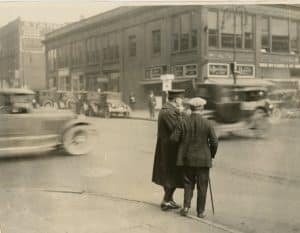 a man crossing a street with a officer. Casper Bihn utilizes a whistle to get assistance crossing a busy Toledo street. Circa 1925.