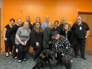 A group photo of a dozen people, all wearing black and looking slick. Also pictured a black Labrador