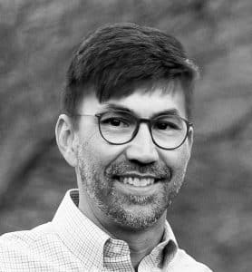 Brian Green - black and white photo of a man smiling and wearing glasses